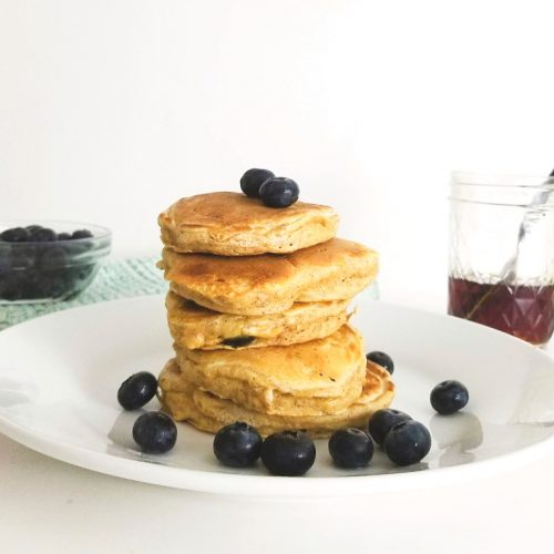homemade blueberry pancakes on a white plate with maple syrup for serving.