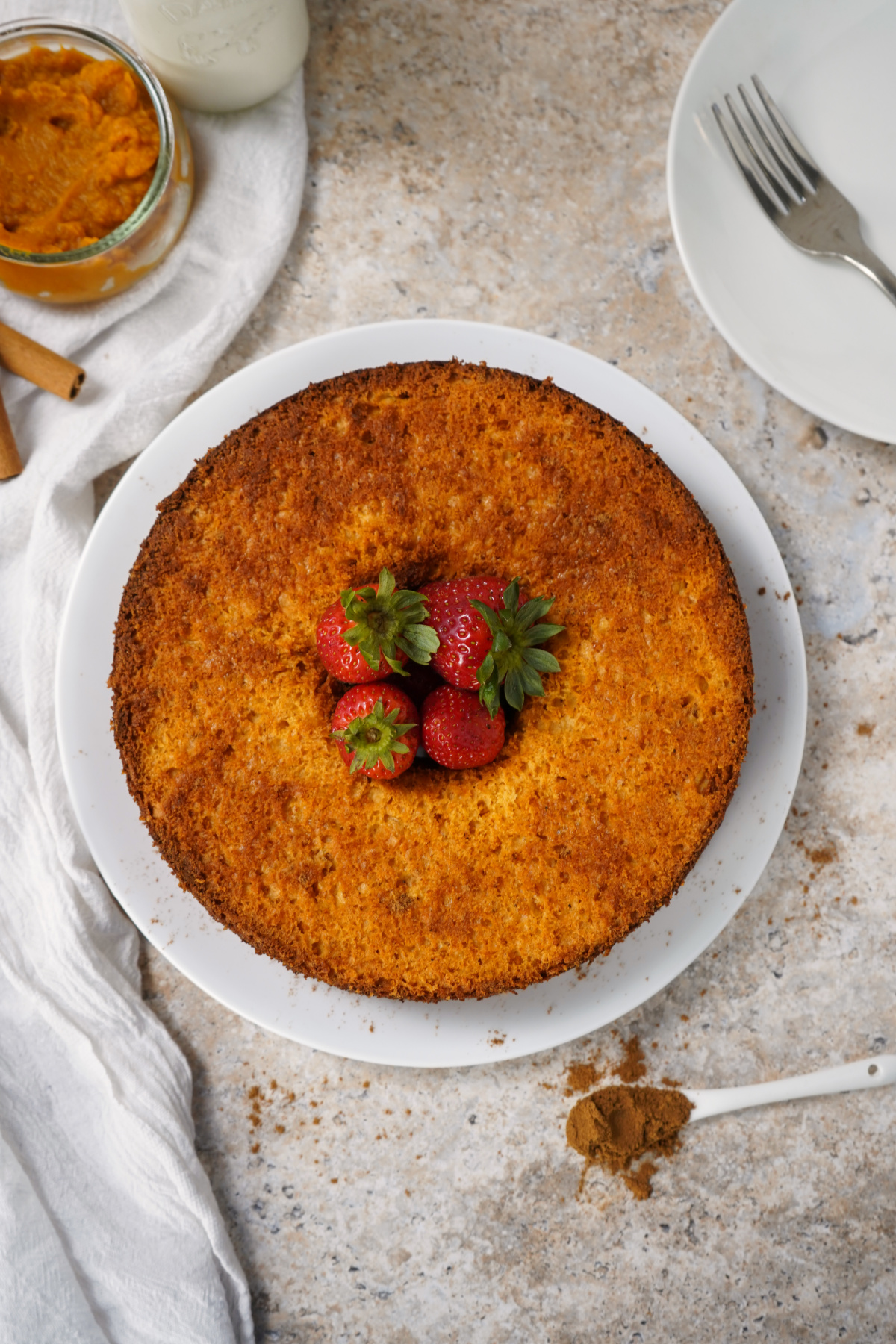 Whole Angel food cake with pumpkin on a white plate with strawberries in the middle