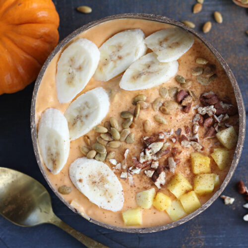 Pumpkin mango watermelon smoothie bowl topped with banana slices, pecans, and cinnamon in a coconut bowl