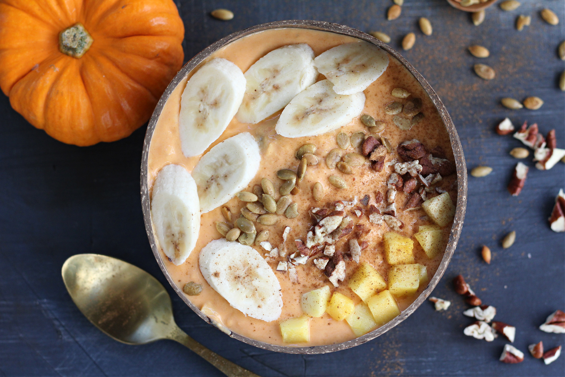 Pumpkin mango watermelon smoothie bowl topped with banana slices, pecans, and cinnamon in a coconut bowl