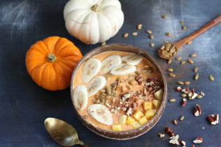 Colorful pumpkin smoothie bowl garnished with pecans, pumpkin seeds, cinnamon, and banana in a rustic coconut bowl