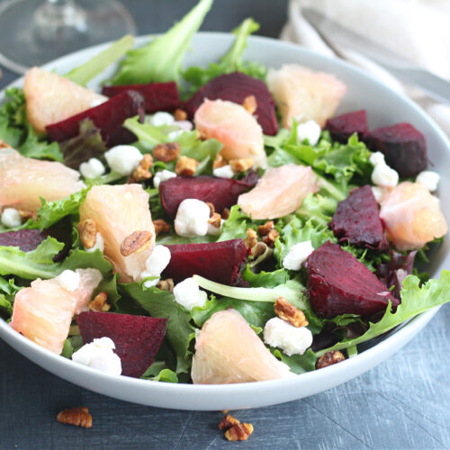 Colorful roasted beet and pummelo salad with goat cheese and walnuts on a light blue bowl