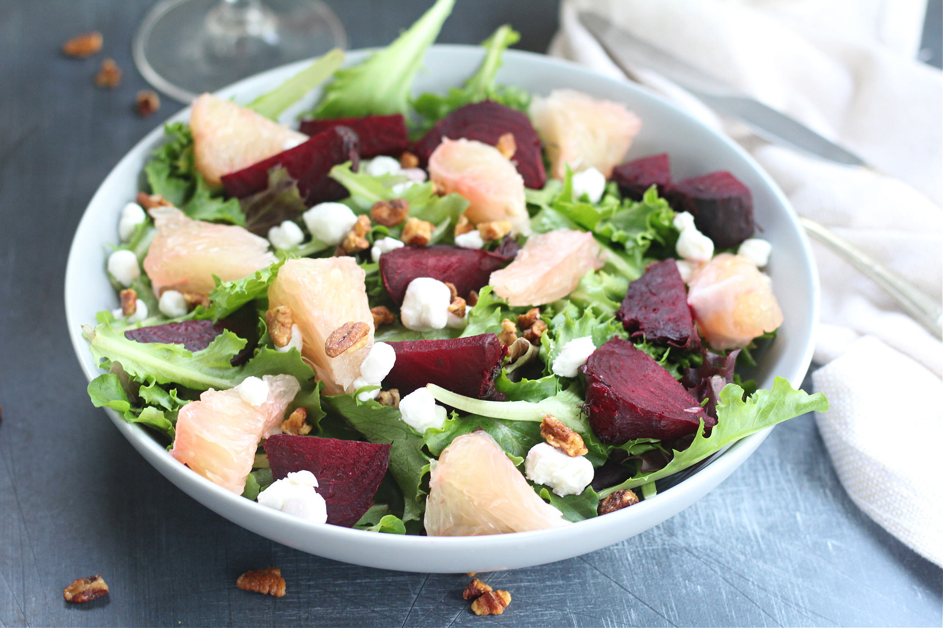 Colorful roasted beet and pummelo salad with goat cheese and walnuts on a light blue bowl