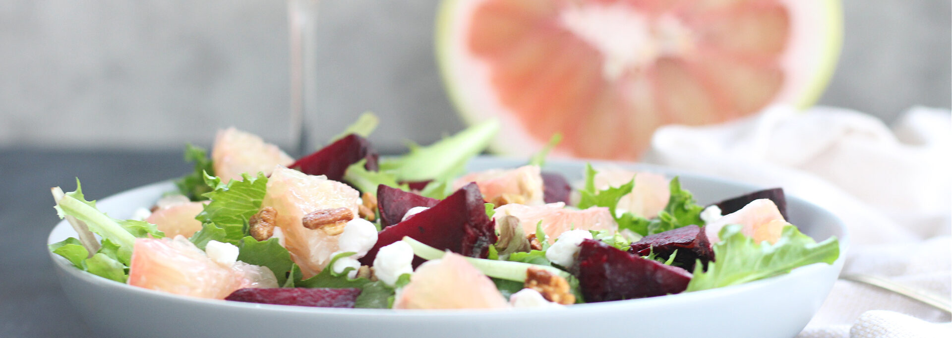Fresh Florida Starburst Pummelo salad with roasted beets, greens, and goat cheese served in a blue bowl with a glass of rose wine and a pummelo in the background