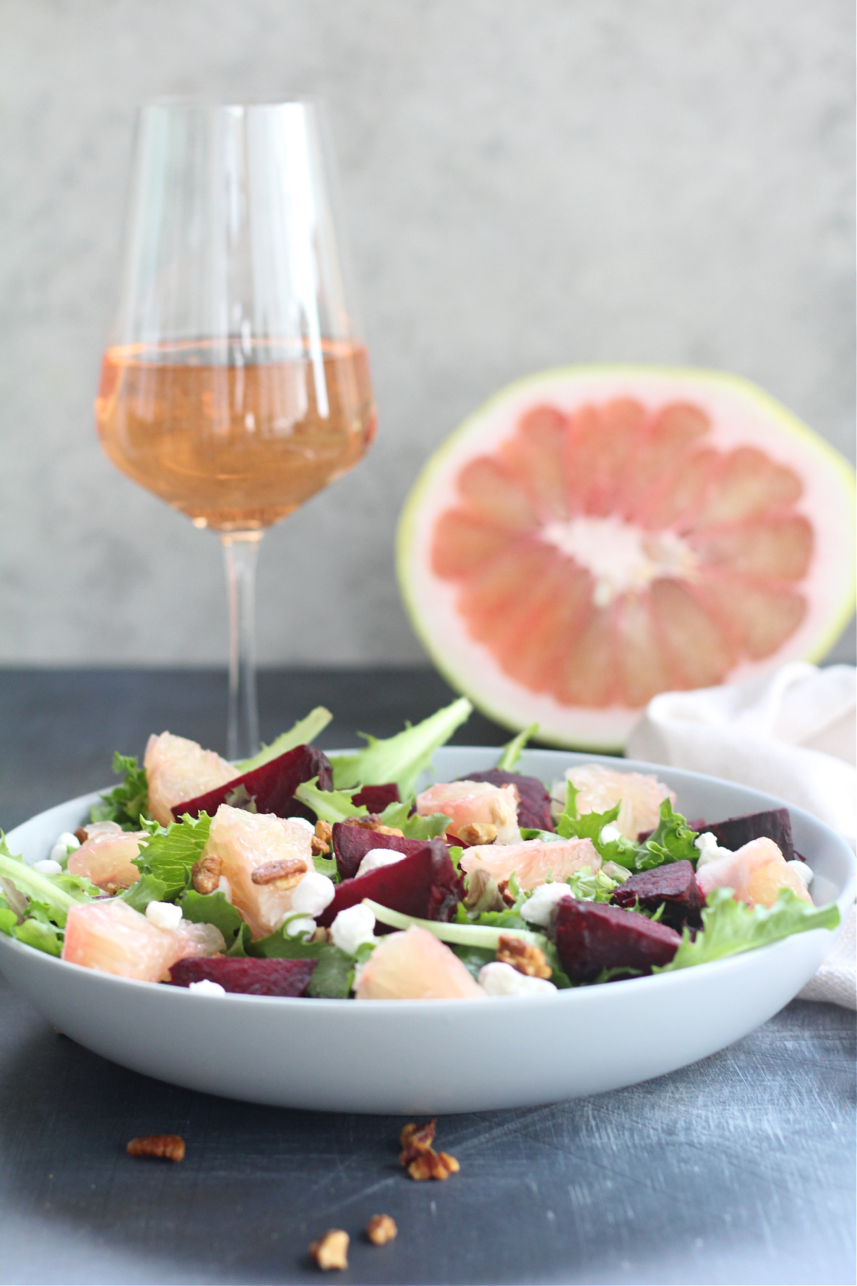 Vibrant winter citrus salad featuring roasted beets, pummelo, goat cheese, and pecans served with a glass of rose wine