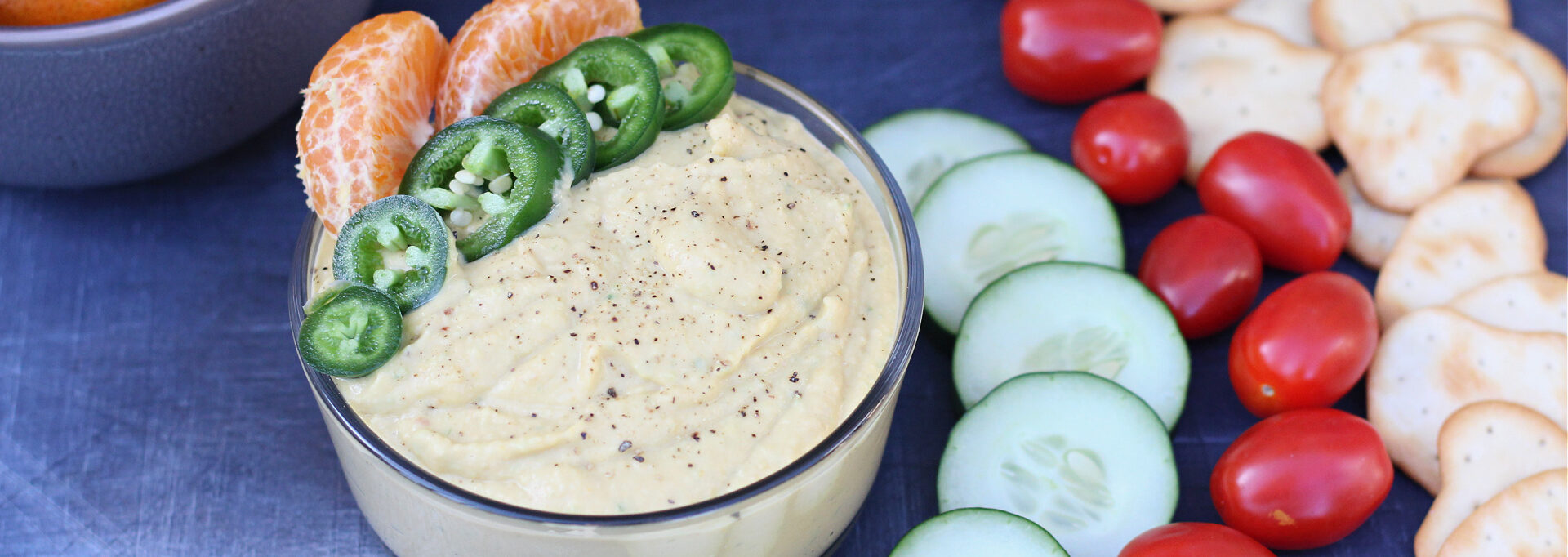 Bowl of homemade spicy tangerine hummus with fresh veggies and crackers for dipping.