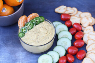 Bowl of homemade spicy tangerine hummus with fresh veggies and crackers for dipping.