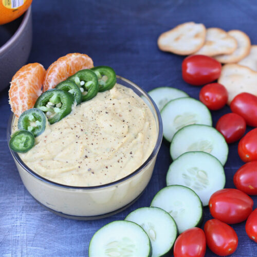 Bowl of homemade spicy tangerine hummus with fresh veggies and crackers for dipping.