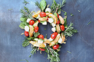 Overhead view of Tangerine Caprese Wreath appetizer arranged with tomatoes, mozzarella, and greens.