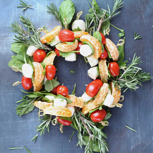 Overhead view of Tangerine Caprese Wreath appetizer arranged with tomatoes, mozzarella, and greens.