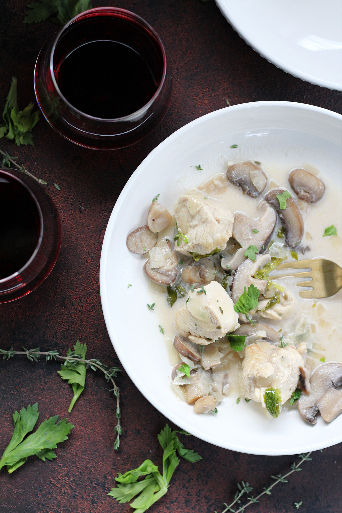 Creamy chicken and mushroom fricassee served in a white bowl served with red wine