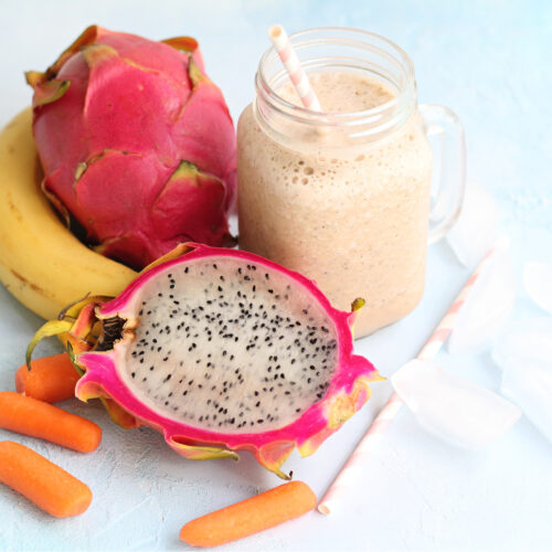 Dragon fruit smoothie in a clear mason jar with tropical fruit and a straw with ice.
