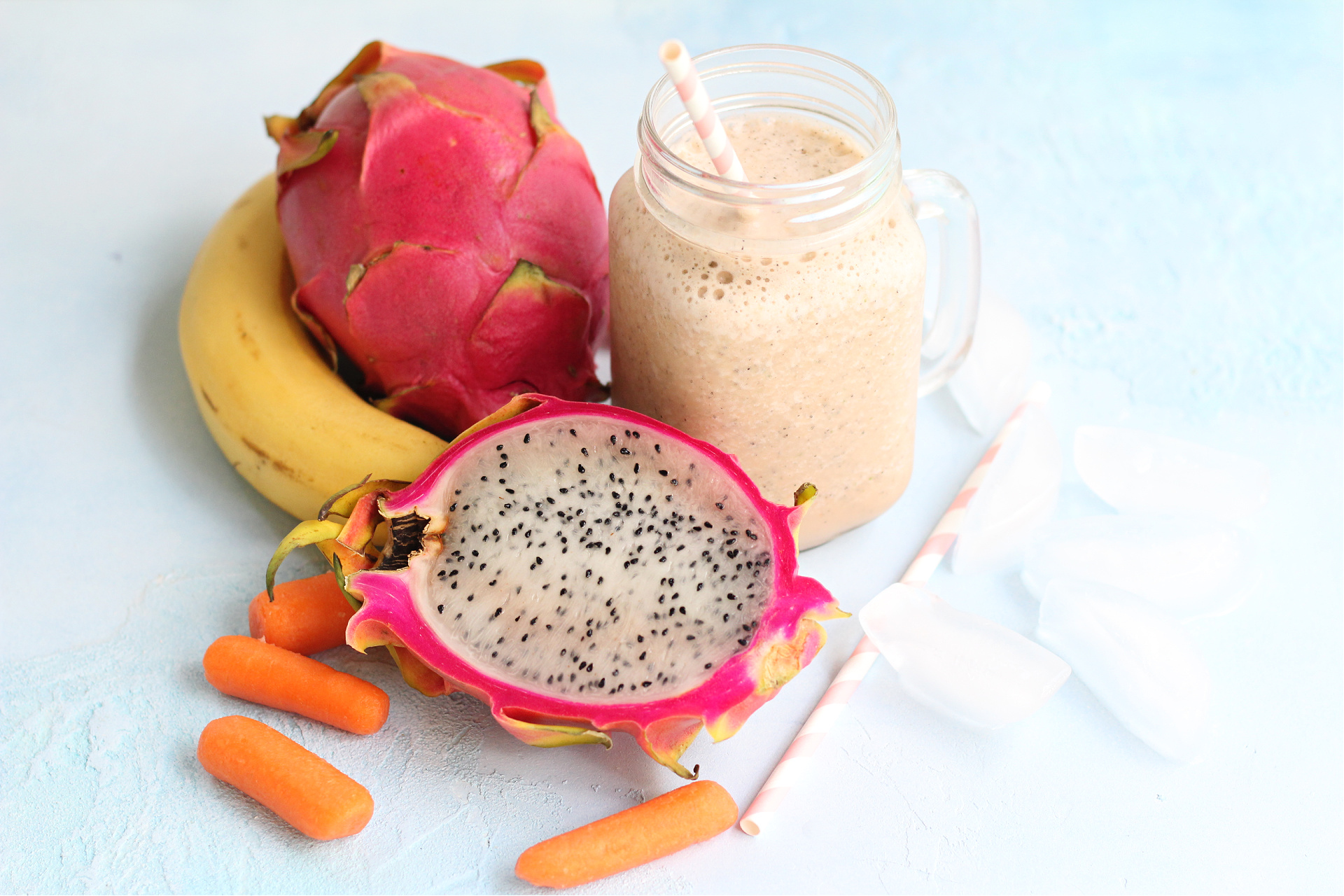 Dragon fruit smoothie in a clear mason jar with tropical fruit and a straw with ice.