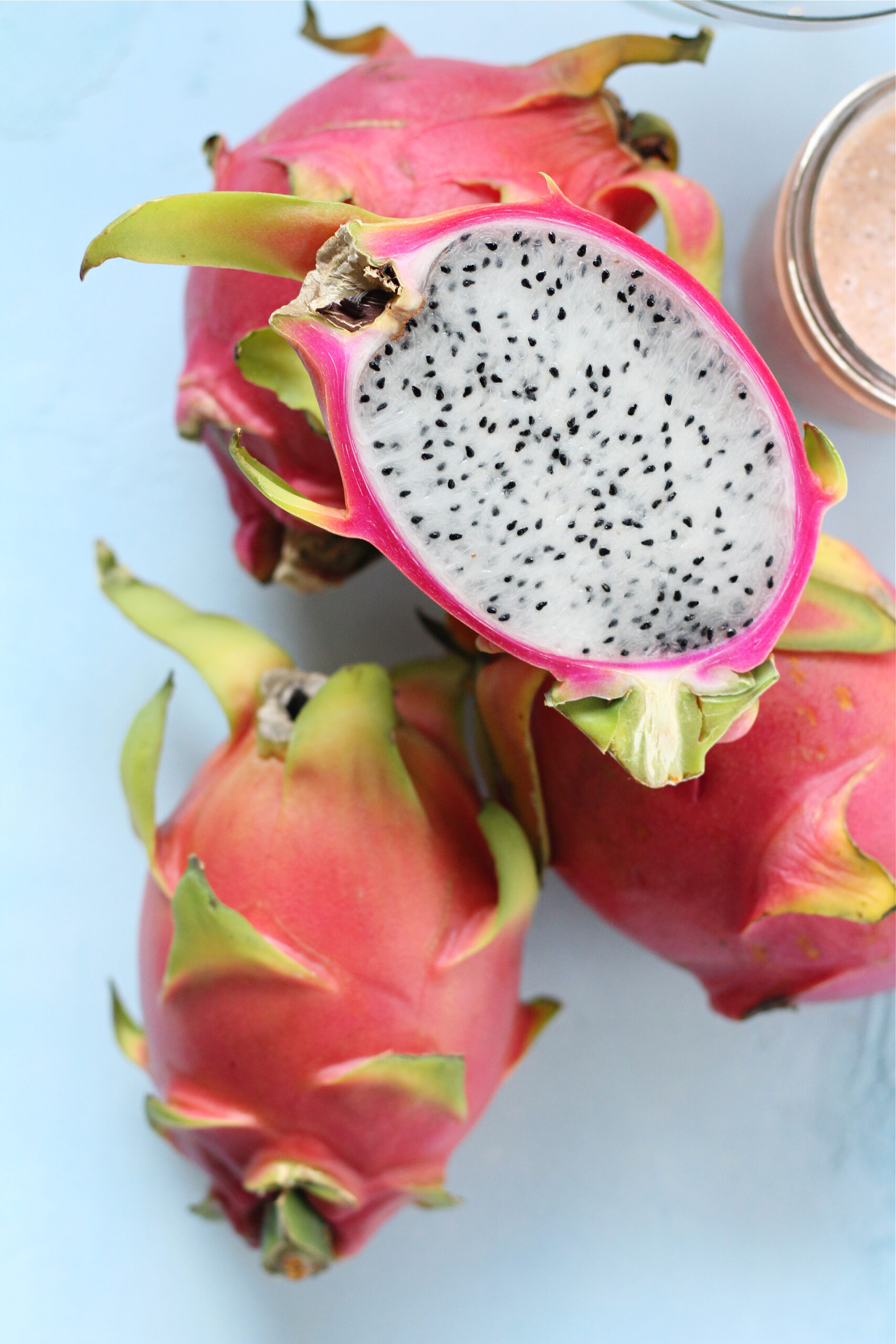 Whole dragon fruit on a counter with one cut open.