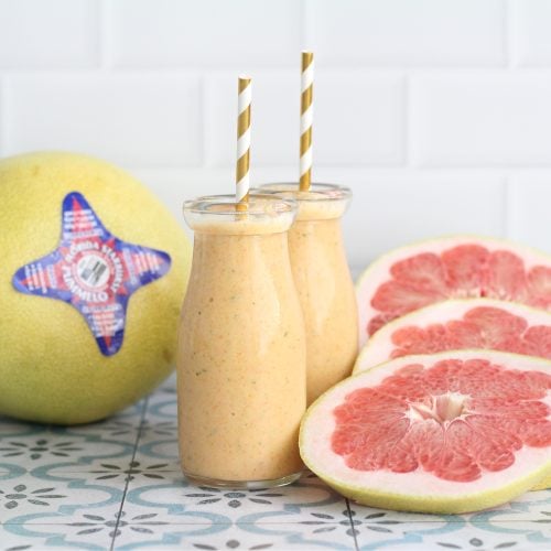 Citrus smoothie with gold straws in the glasses with an pummelo slices and a whole pummelo in the background.