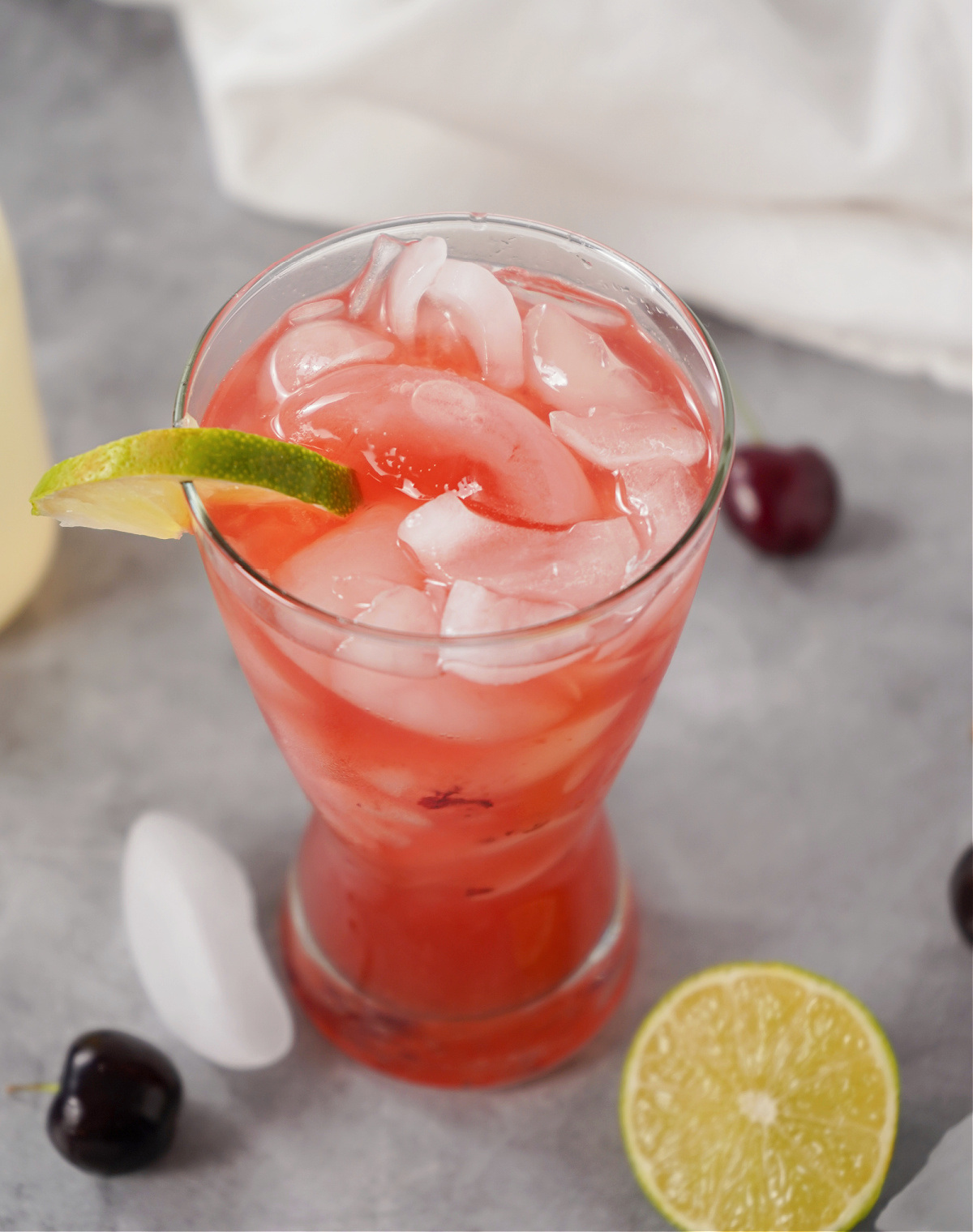 Sparkling Ros&eacute; Cherry Lemonade Spritz cocktail garnished with lime and surrounded by fresh cherries.