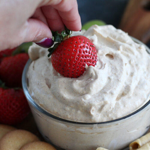 Hand dipping a strawberry into a bowl of pumpkin fluff dip.