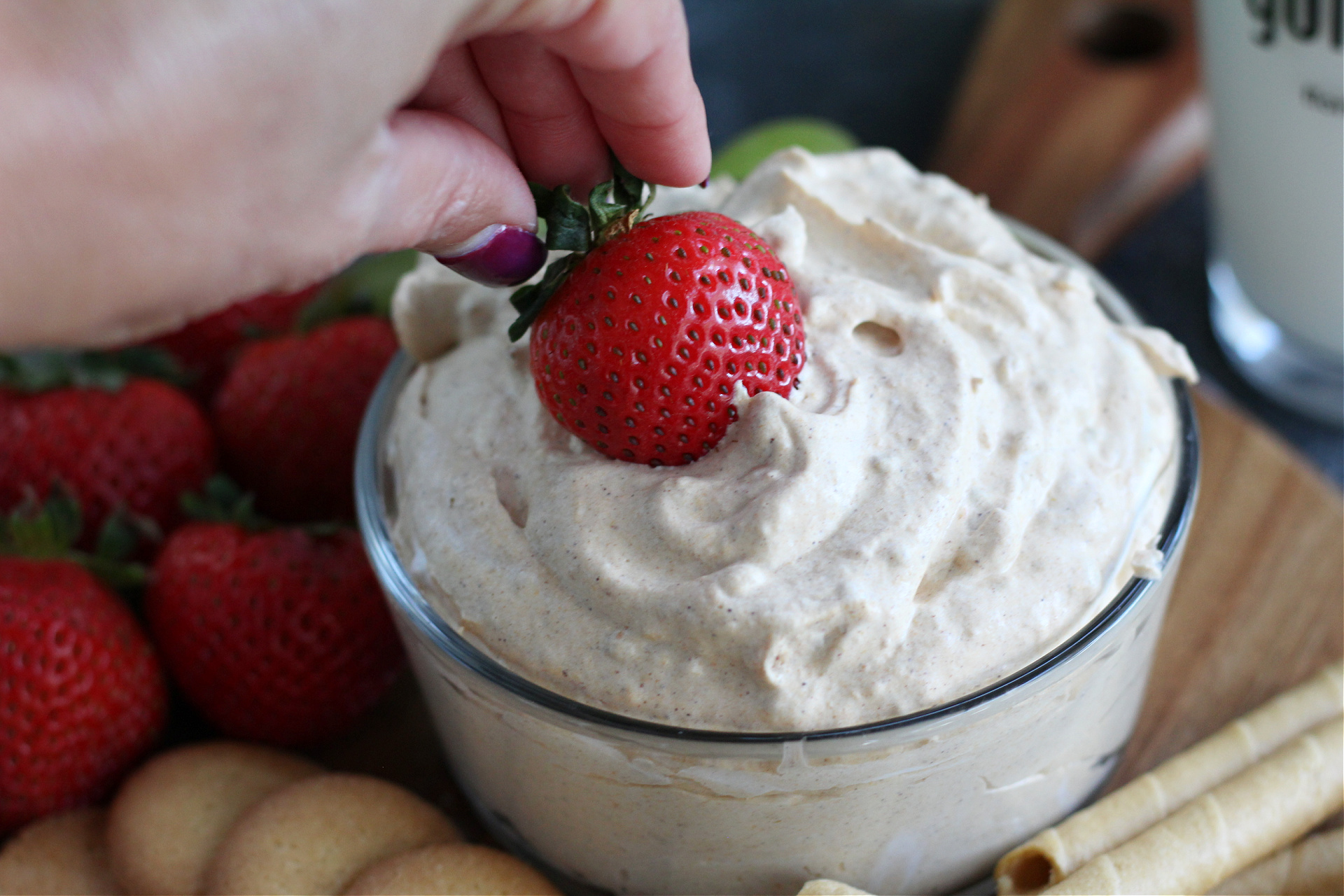 Hand dipping a strawberry into a bowl of pumpkin fluff dip.