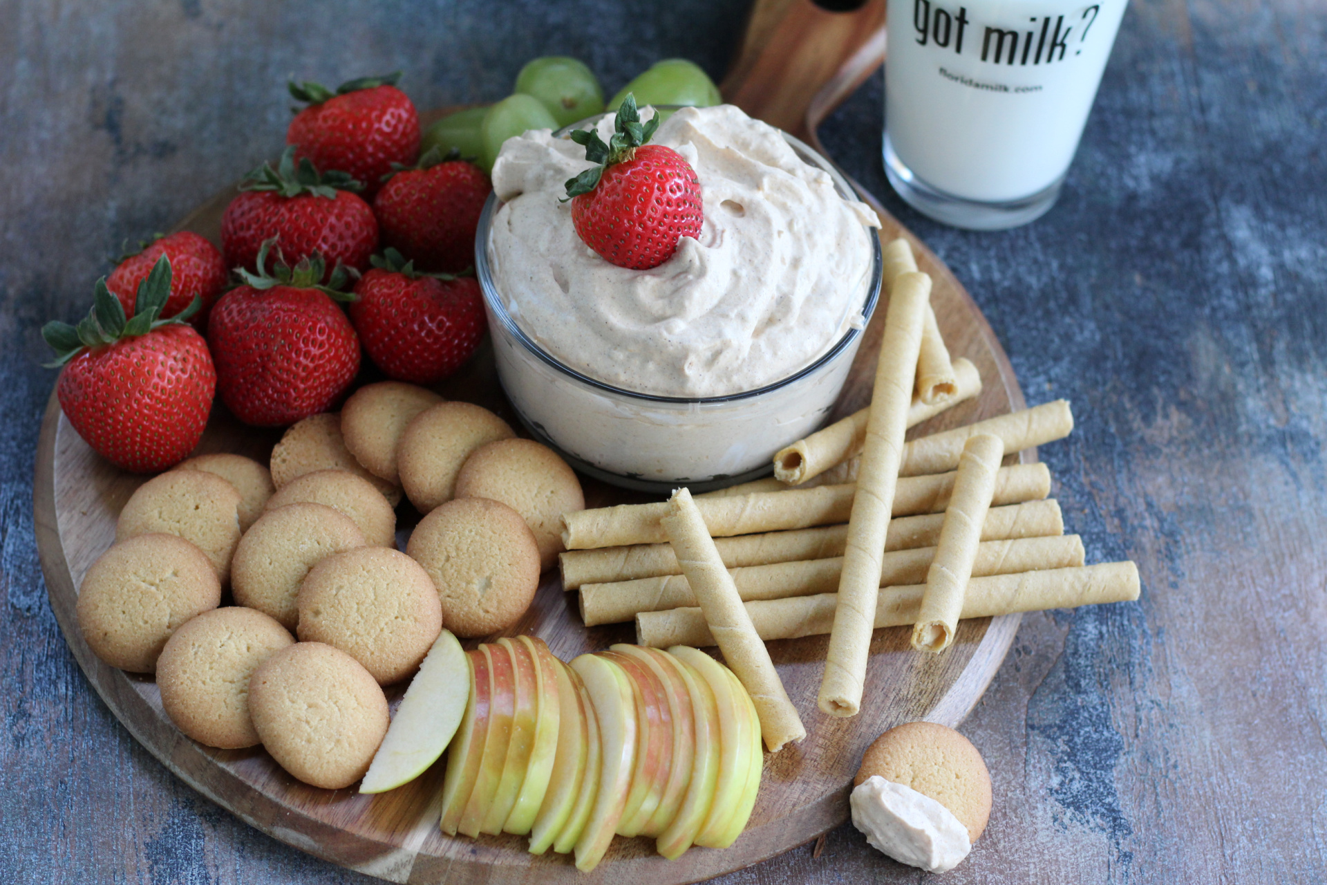 Creamy pumpkin fluff dip in a bowl with with cookies and fruit around it served with a glass of milk.