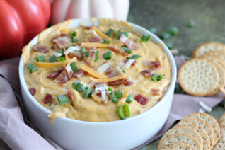 Creamy savory pumpkin dip with bacon and cheese surrounded by crackers for dipping