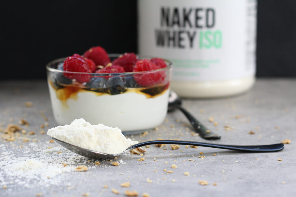 Scoop of vanilla protein powder beside yogurt and fresh fruit.