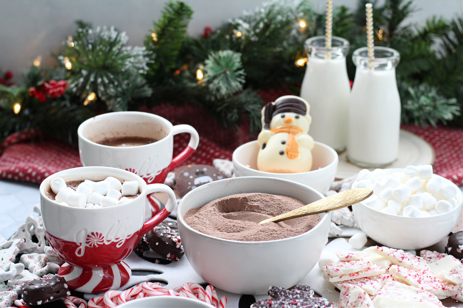 Festive mugs of peppermint hot chocolate topped with marshmallows on a dessert board.
