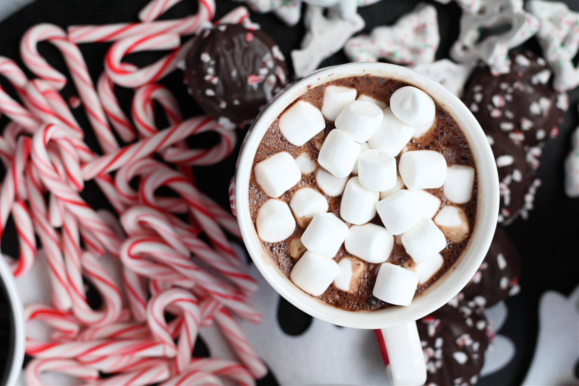 Close-up of a holiday-themed hot cocoa board featuring assorted toppings like peppermint candies, chocolate cups, and seasonal sweets for DIY cocoa.