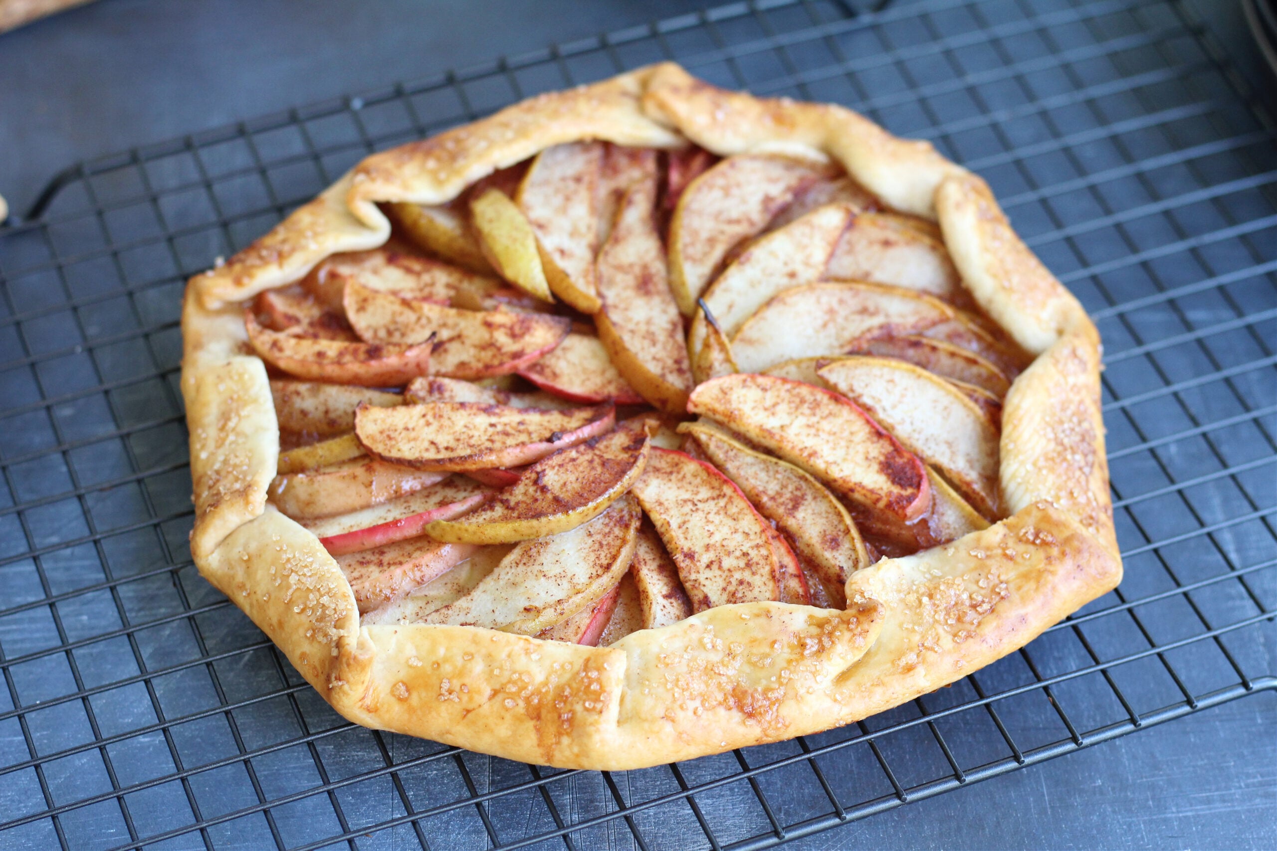Rustic apple and pear galette on a cooling rack with golden brown crust and cinnamon-spiced fruit slices.