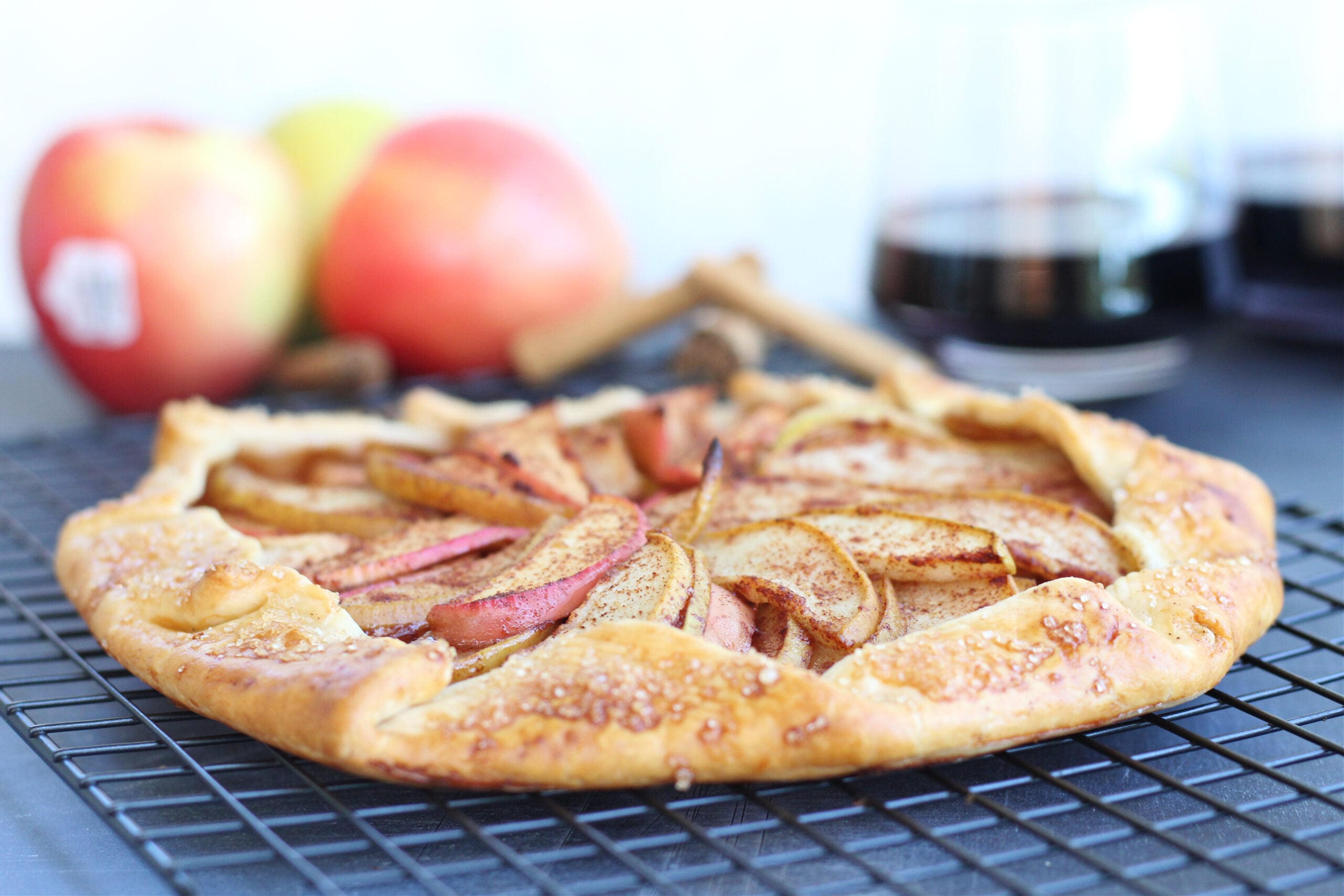 Fresh apple and pear beside a baked apple and pear galette on a cooling rack.