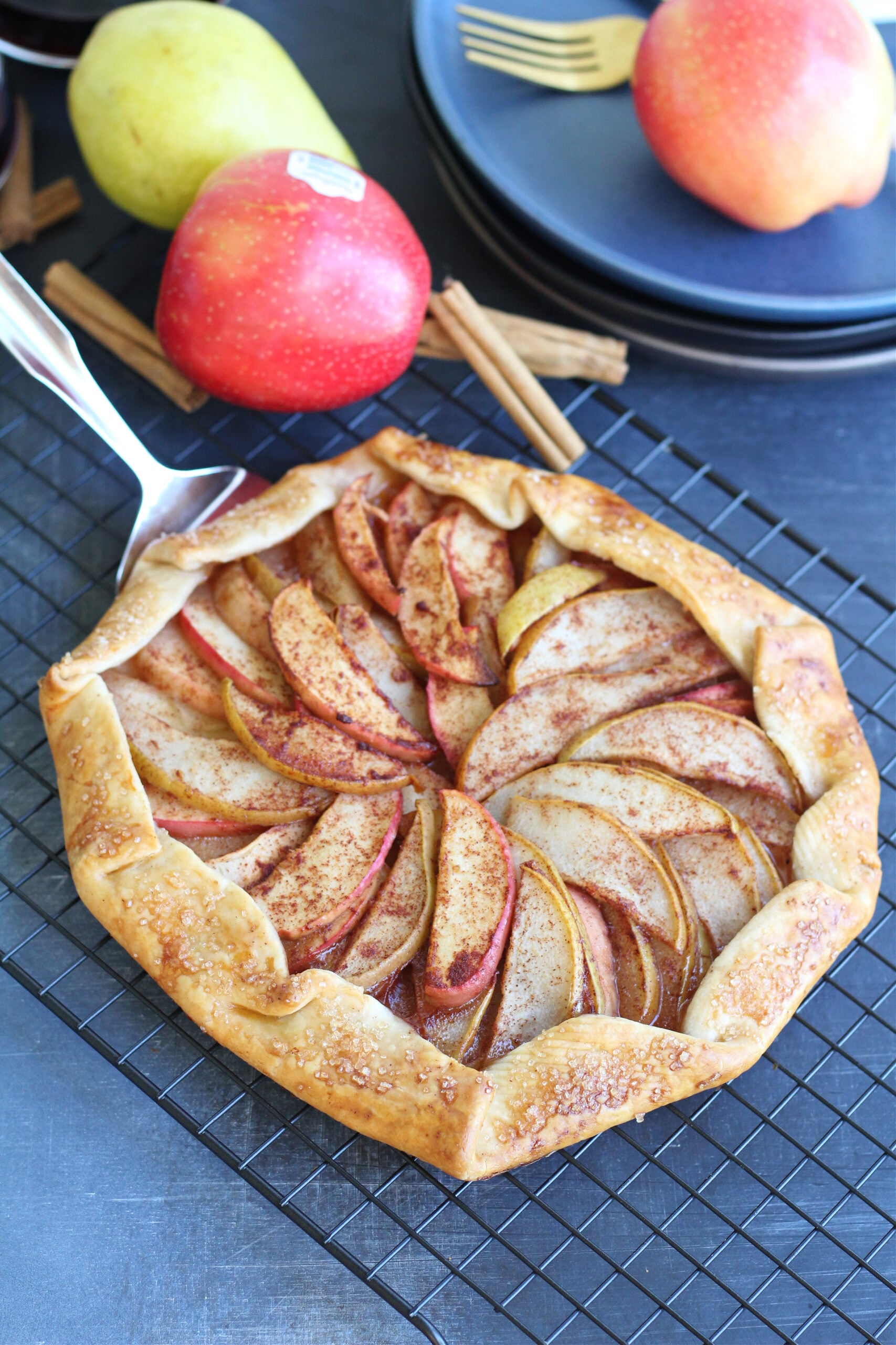 Apple and pear galette cooling next to plates and gold flatware ready for serving.