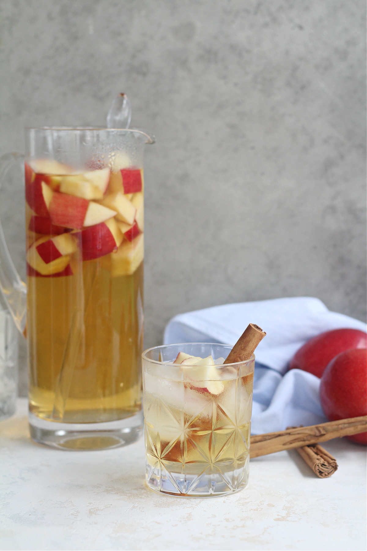 Glass pitcher filled with sliced apples and white wine apple sangria with cinnamon sticks.
