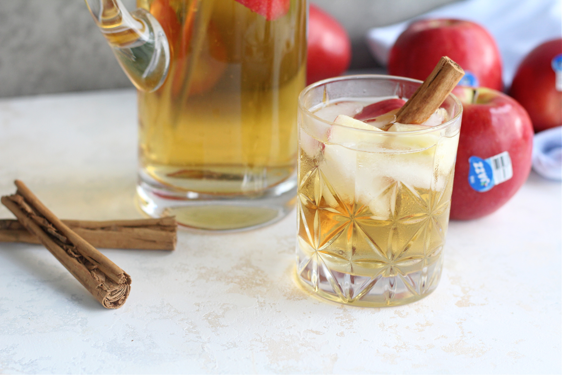 Apple slices and cinnamon sticks floating in golden apple sangria in a glass.