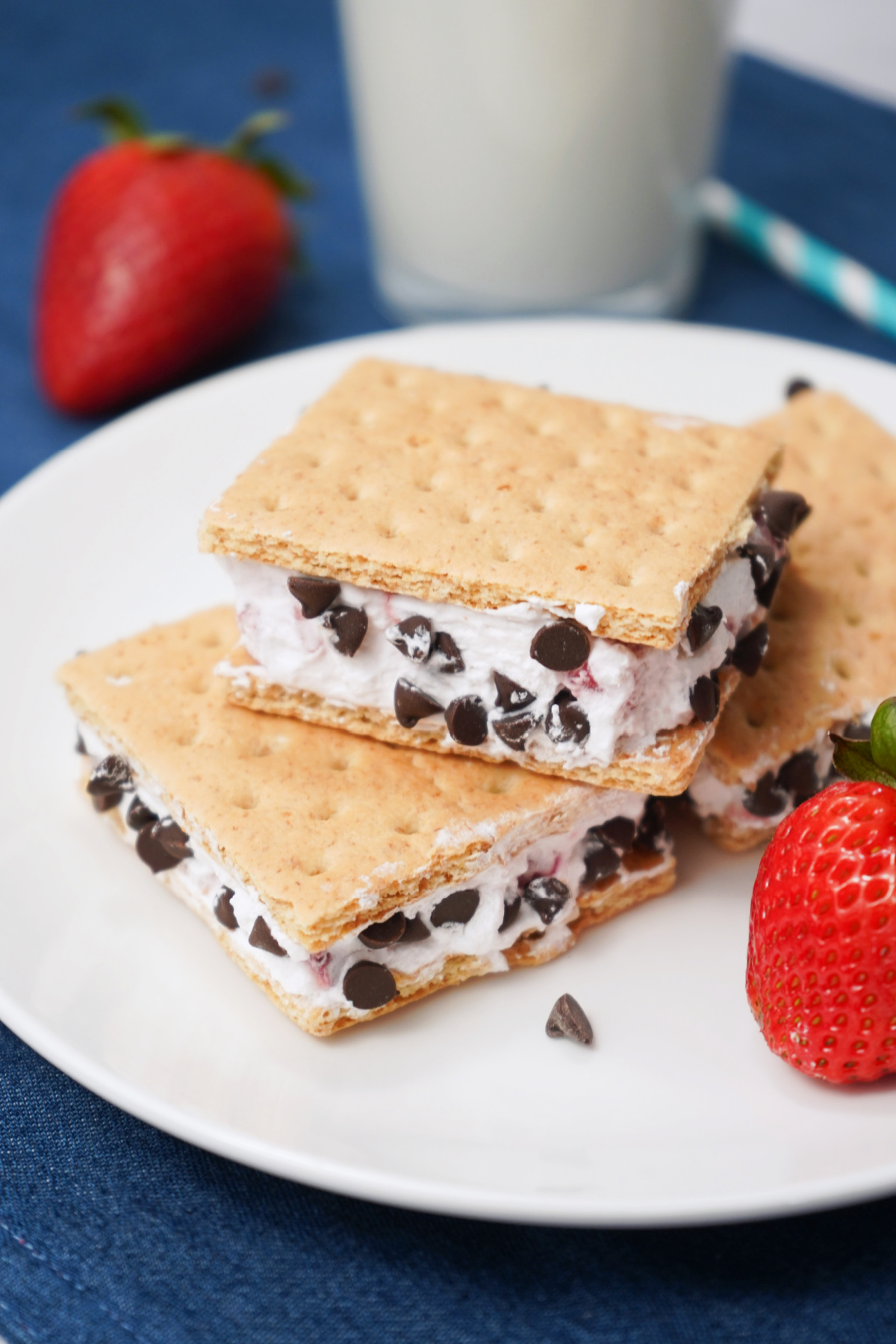 Homemade Cool Whip ice cream sandwiches stacked with fresh strawberries in the background.
