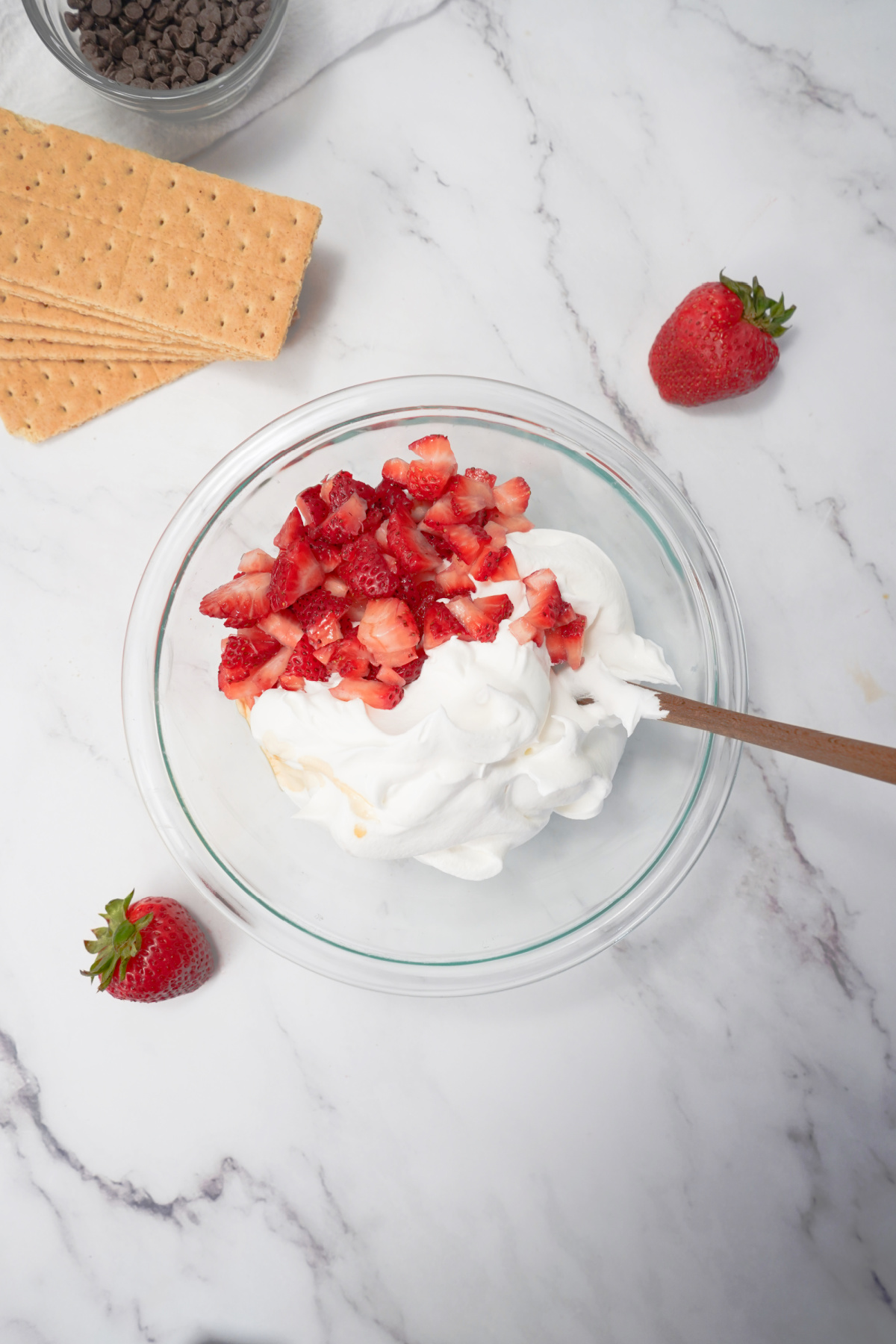 Mixing creamy Cool Whip mixed with fresh strawberries for graham crackers to assemble frozen ice cream sandwiches.