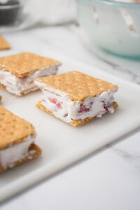 Spreading creamy Cool Whip mixed with fresh strawberries onto graham crackers to assemble frozen ice cream sandwiches.