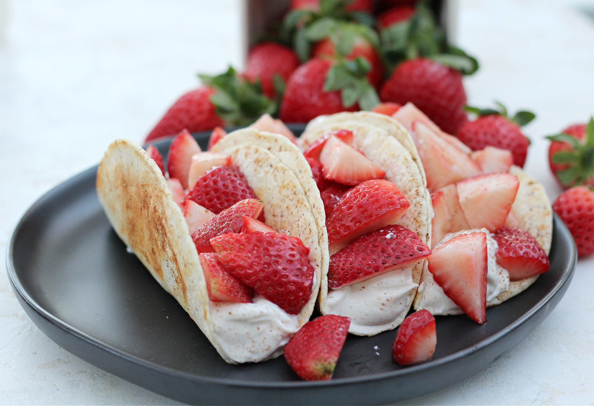 Strawberry breakfast tacos arranged on a plate with fresh strawberries