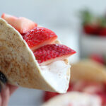 Close-up of strawberry cheesecake–style tacos topped with fresh sliced strawberries