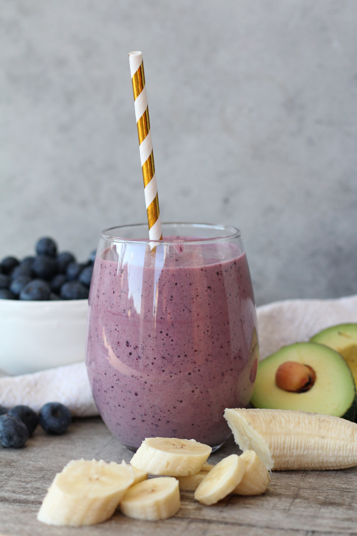 Blueberry avocado smoothie in a glass with fresh fruit on a wooden surface