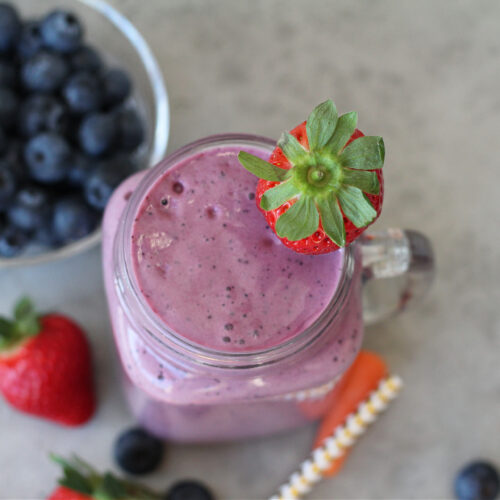 Purple carrot blueberry smoothie surrounded by fresh fruit and vegetables