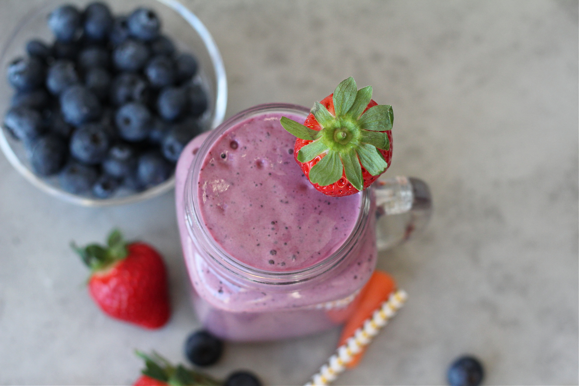 Purple carrot blueberry smoothie surrounded by fresh fruit and vegetables