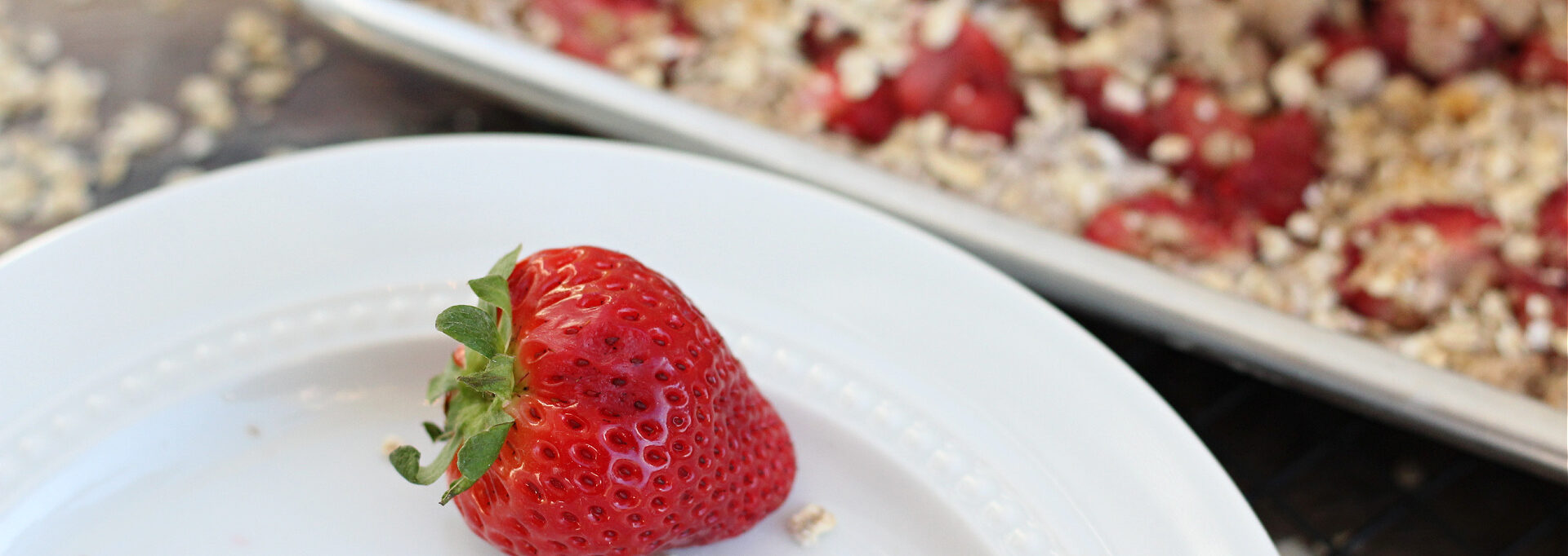 Close-up of juicy strawberry with oatmeal bars on a baking sheet in the background