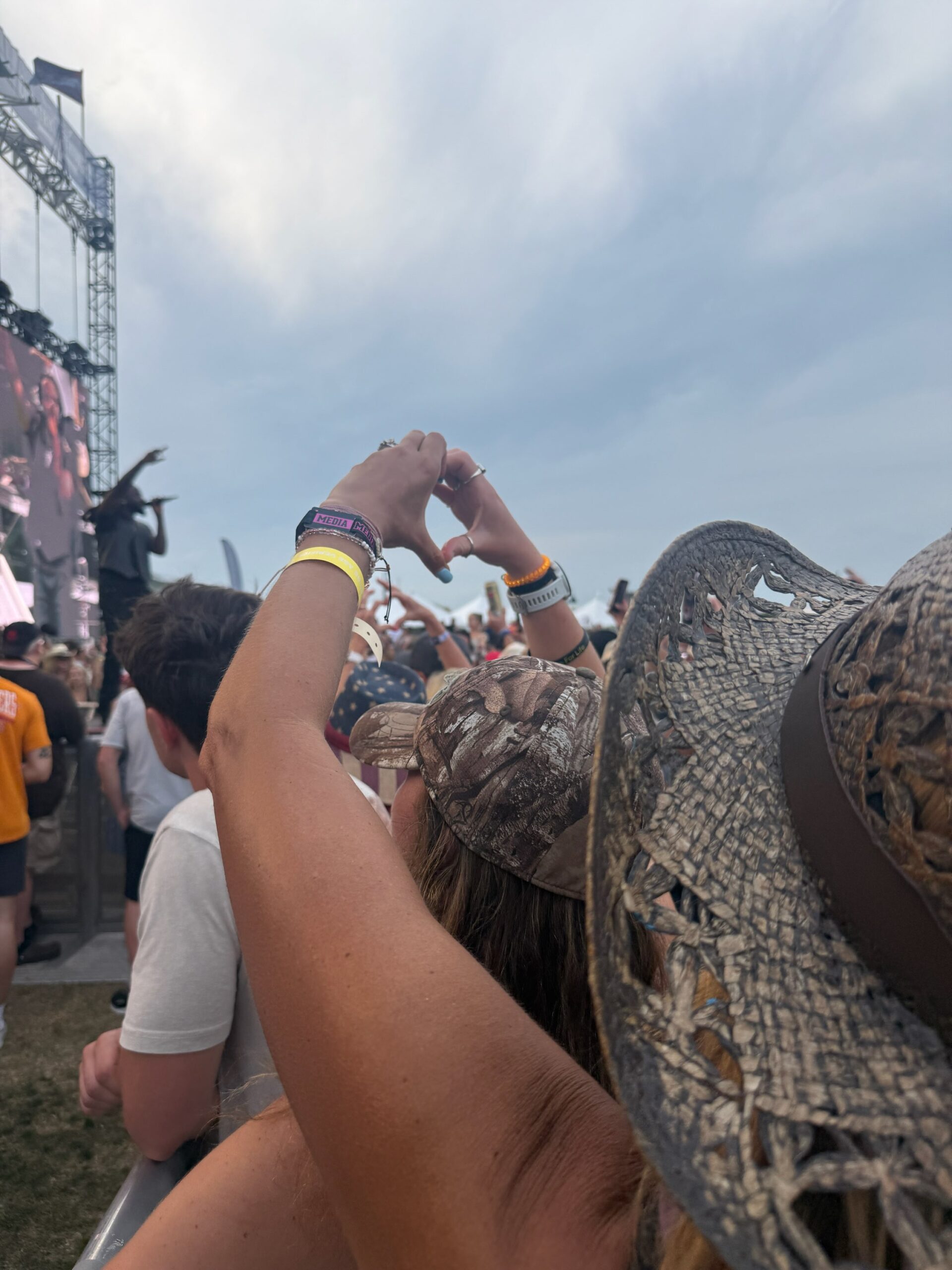 Mother and daughter making a heart shape with their hands while watching Shaboozey perform at Country Thunder Florida, surrounded by country music festival crowds and camo cowboy hats.